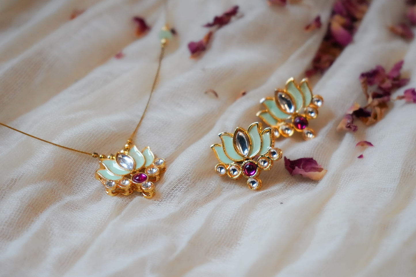 Decorative earrings with gold and gemstone details on a soft fabric background.