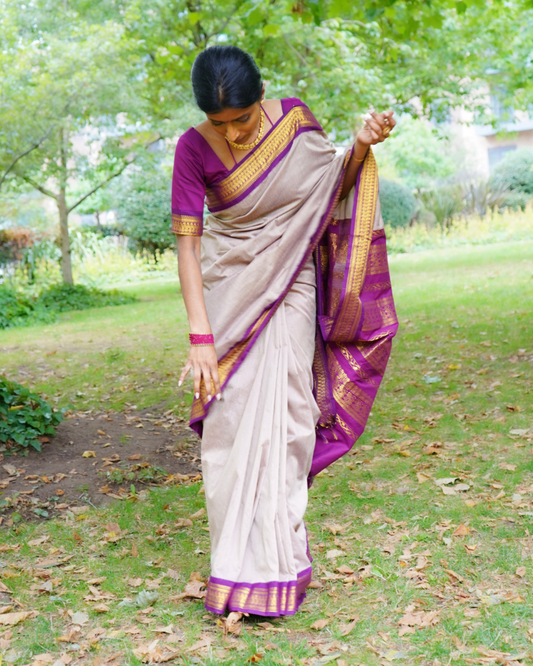 Woman in a traditional saree standing outdoors on a grassy area with trees in the background
